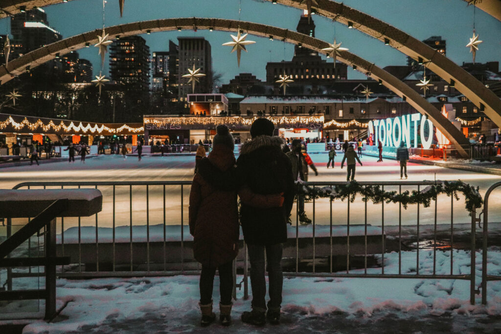 two friends with their backs to the camera, checking out a festive outdoor skating rink