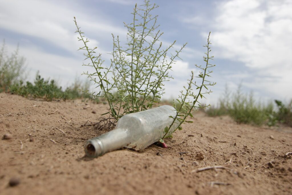 A dusty glass bottle on sandy dry ground under a wide blue sky. 