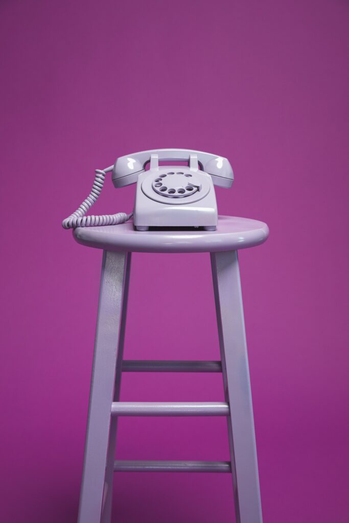 An old fashioned purple rotary telephone on a purple painted stool. 
