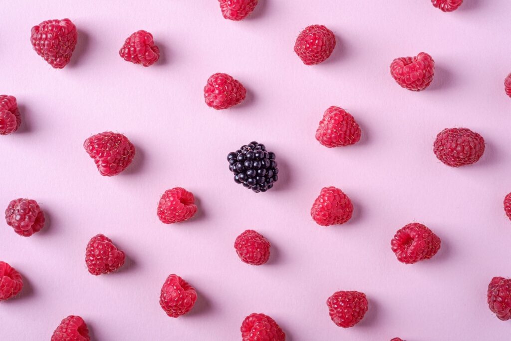 Fresh raspberries and one blackberry on a pale pink background. 