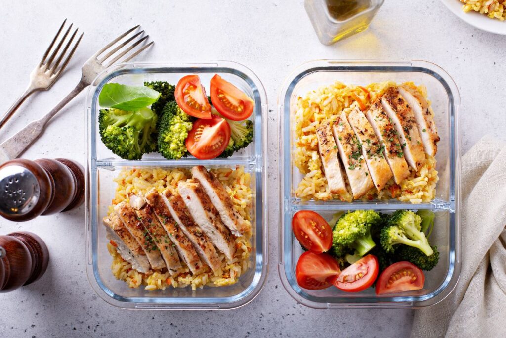 two class meal prep containers with chicken, rice, broccoli, and tomatoes 