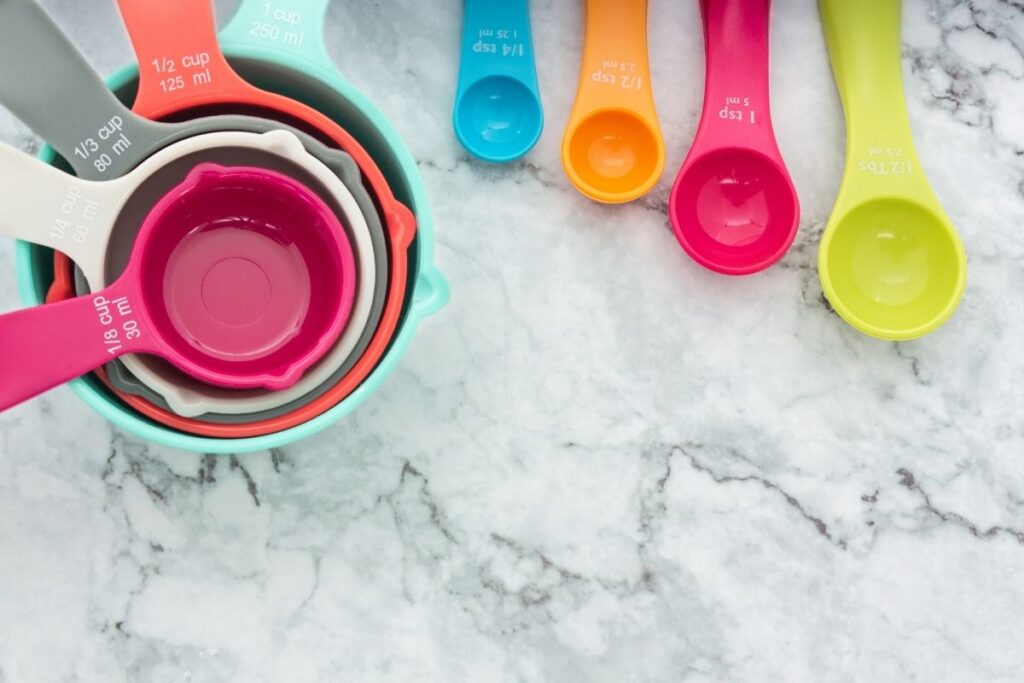 five different measuring cups for gastric sleeve meal size that are 1/8 cups, 1/4 cup, 1/3 cup, 1/2 cup, and 1 cup as well as measuring spoons 1/4 tsp, 1/2 tsp, 1 tsp, and 1 tbsp displayed on a granite counter top