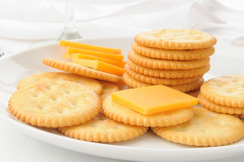 white plate with round golden brown rackers stacked on top with thin slices of cheddar cheese to explain why can't we eat crackers after bariatric bypass surgery